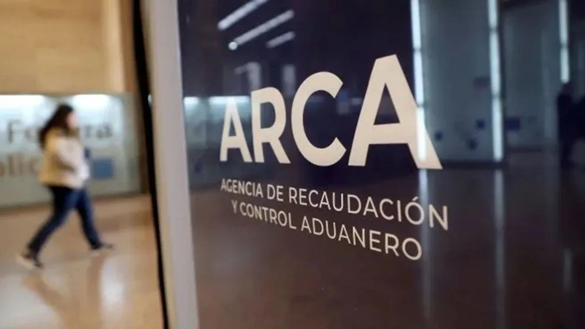 Cartel con el logo de ARCA, Agencia de Recaudación y Control Aduanero, en el hall de una de sus oficinas; detrás pasa una mujer