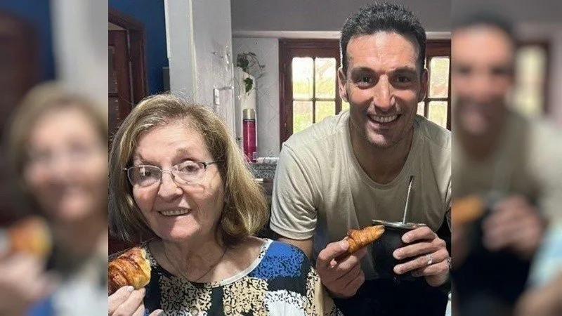 Una mujer mayor con anteojos y un hombre de pelo corto sonríen a cámara en una cocina; ambos sostienen medialunas y él tiene un mate en la mano.