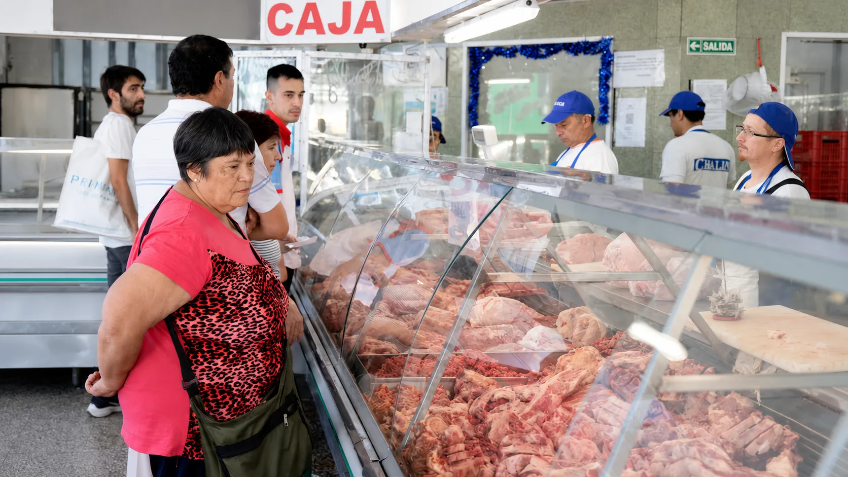 Clientes frente al mostrador de una carnicería, con los carniceros atendiendo detrás de la vitrina