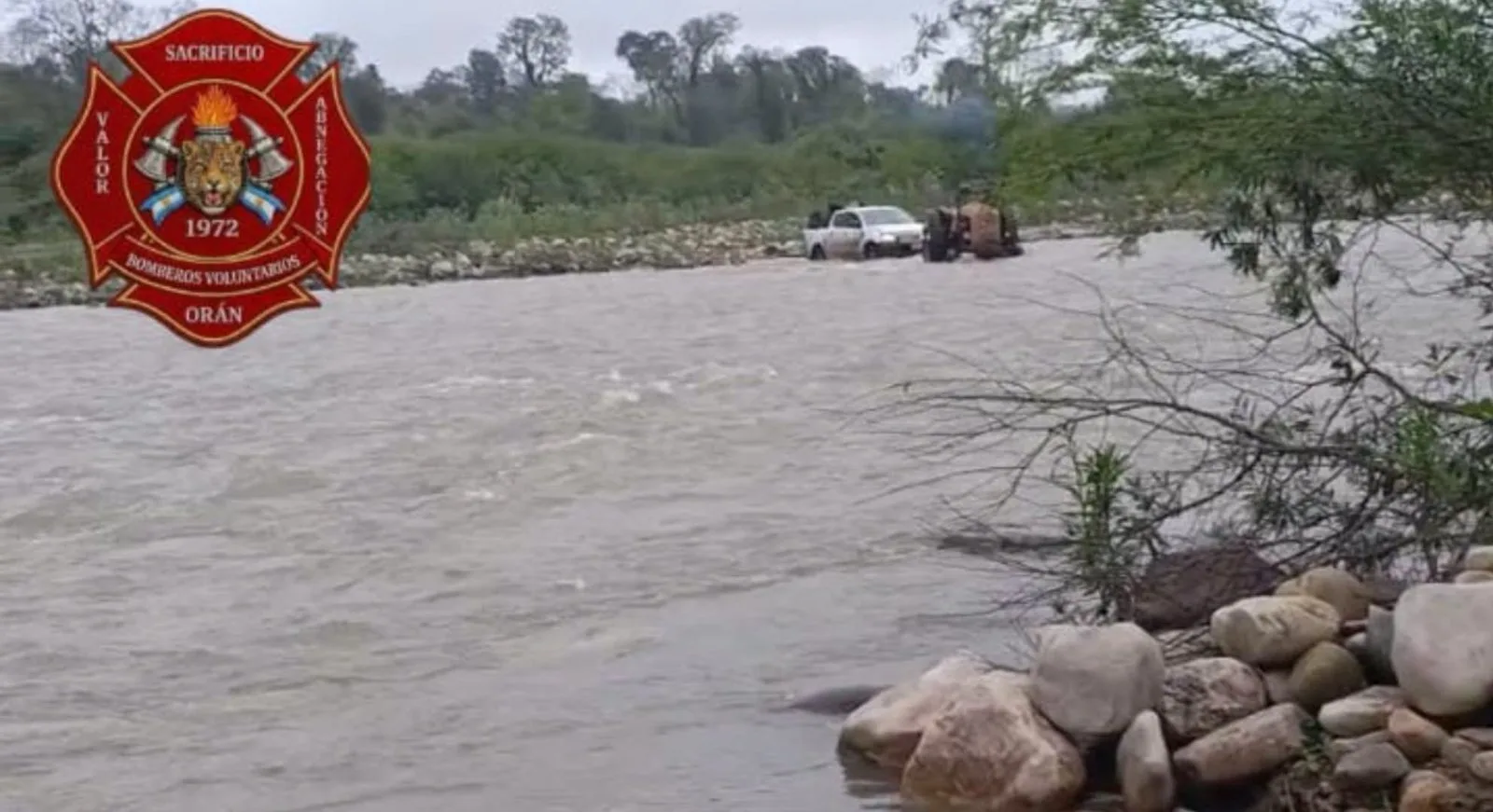 Una camioneta blanca y un tractor en el cruce de un río crecido del norte de Salta, en la foto de Bomberos Voluntarios de Orán