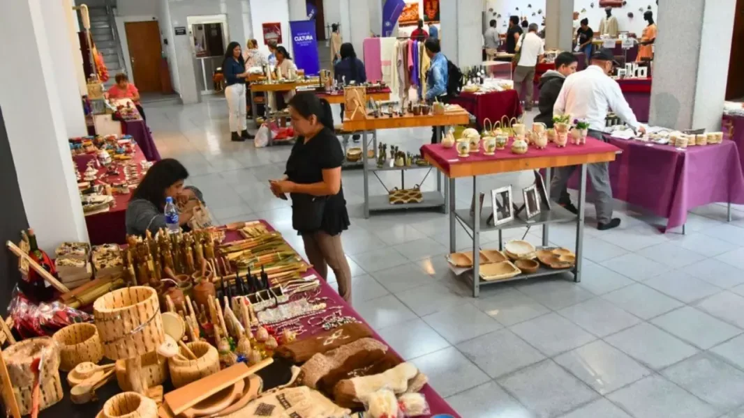 Puestos de la feria artesanal en la Casa de la Cultura con cestería, cerámica, tejidos y visitantes recorriendo las mesas