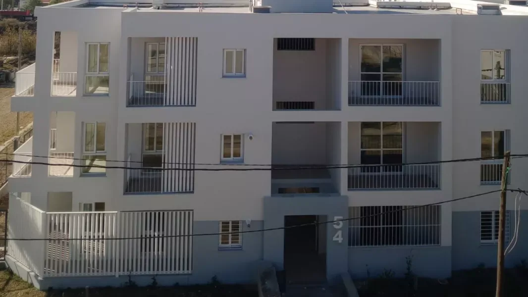 Fachada de un bloque de departamentos de tres plantas recién terminado, con balcones de rejas blancas y el número 54 sobre el ingreso