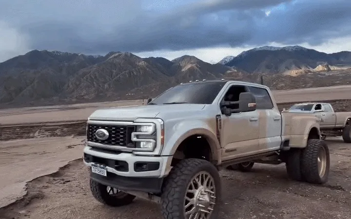 Camioneta pickup modificada, con suspensión elevada y ruedas gigantes, de la caravana brasileña en un camino de tierra con montañas de fondo