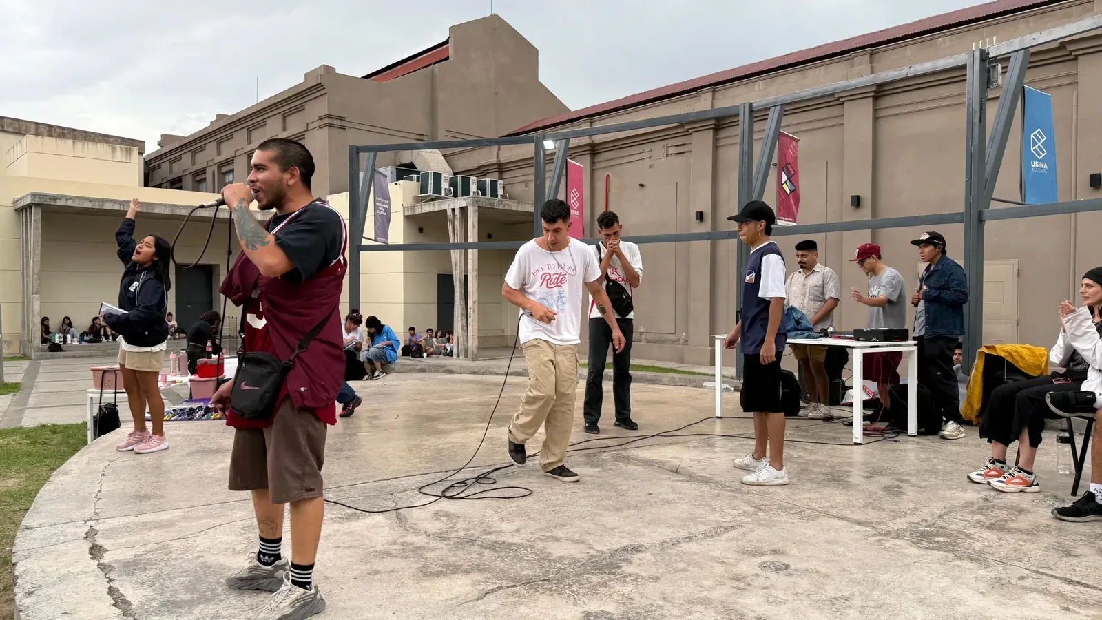 Un joven rapea con micrófono en el patio de la Usina Cultural mientras un grupo de asistentes lo escucha