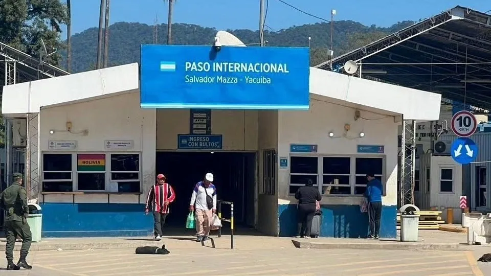 Edificio del paso internacional Salvador Mazza - Yacuiba, con el cartel azul de ingreso y personas cruzando con bolsas