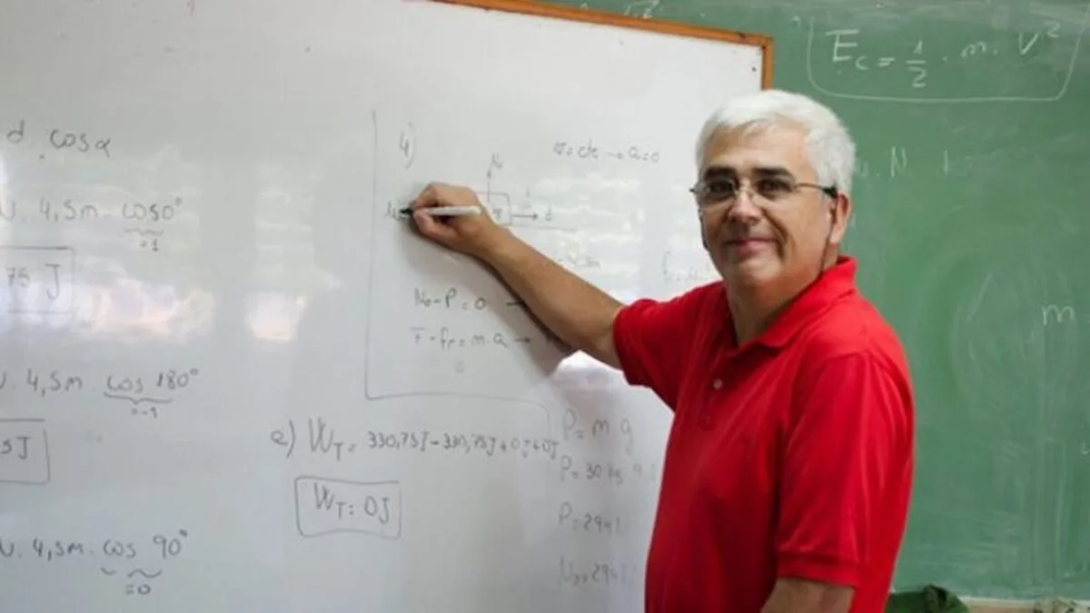 El profesor Daniel Córdoba, de chomba roja, escribe ecuaciones de física en un pizarrón blanco
