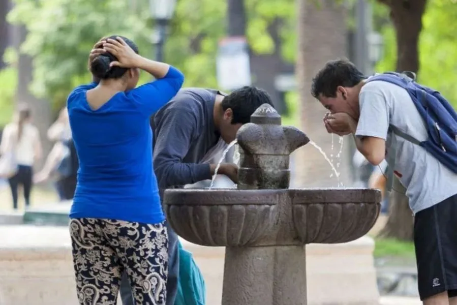 Tres personas se refrescan en un bebedero de plaza en un día de calor