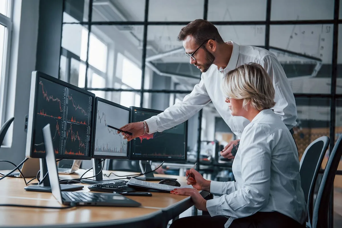 Dos personas analizan gráficos financieros en varios monitores de una oficina