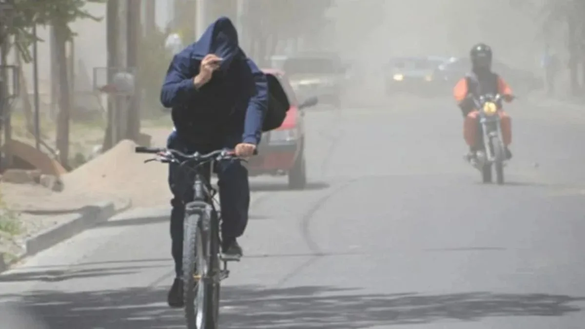 Un ciclista se cubre la cara con la capucha en una calle envuelta en polvo durante un día de viento Zonda